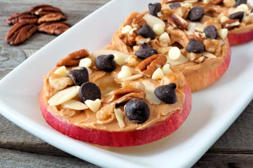 Apple slices topped with peanut butter, nuts, and chocolate chips.