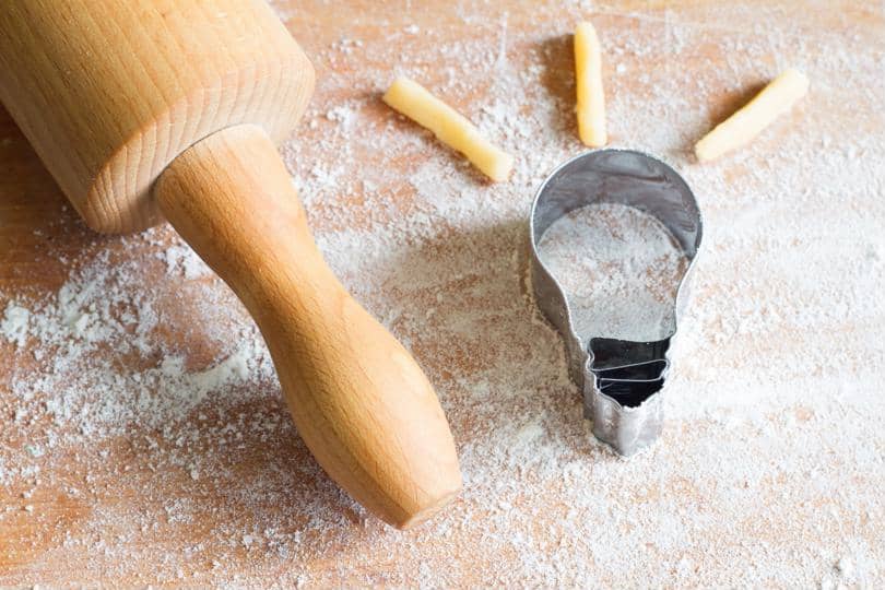 A rolling pin and lightbulb-shaped cookie cutter appear on a floured work surface.